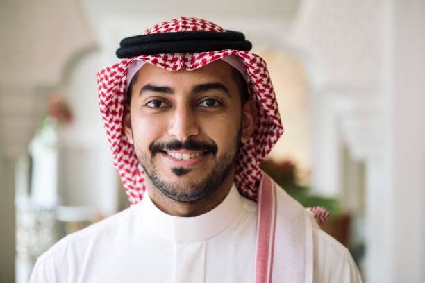 istockphoto-1394149742-612×612 Head and shoulder view of Middle Eastern man wearing traditional dish dash, kaffiyeh, and agal and smiling at camera.